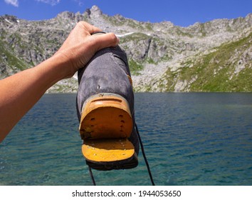 A Woman's Hand Holding A Broken Hiking Boot While Walking. In The Background - Lago Gelato, Madonna Di Campiglio, Italy.