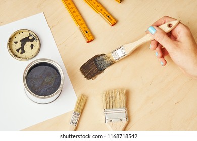 woman's hand is holding a brush with paint and painting a wooden table