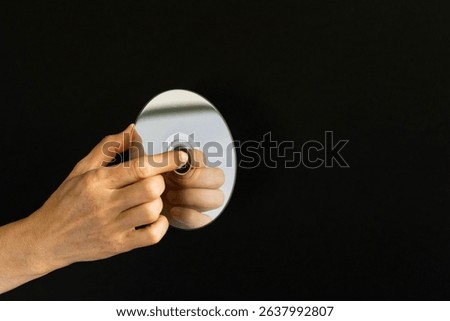 Woman's hand is holding a CD, compact disc. Shiny CD in hand and dark background.