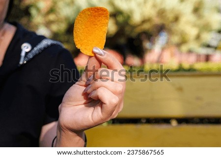 Woman's hand holding chips, snack and fast food concept. Selective focus on hands with blurred background and copy space for text.