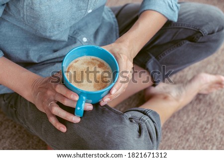Woman's hand holding a cup of coffee. Young woman sitting on the floor. Girl drinking coffee or tea sitting cozy at home. Relax and rest. Closeup.