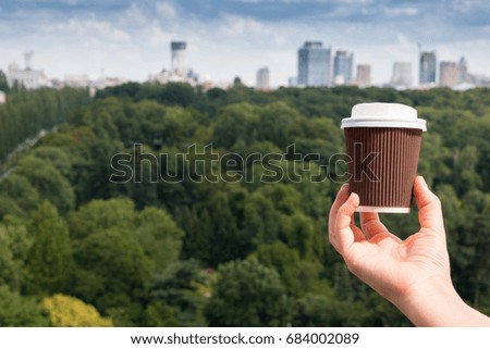 Woman's hand holding a cup of coffee by the view of green park and city
