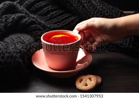 Woman's hand holding cup of tea with lemon on dark background