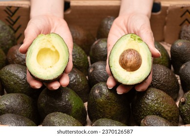 Woman's hand holding a cut avocado - Shutterstock ID 2370126587
