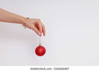 Woman's Hand Holding Decorative Red Christmass Ball Over The White Wall. Minimalist Decor.