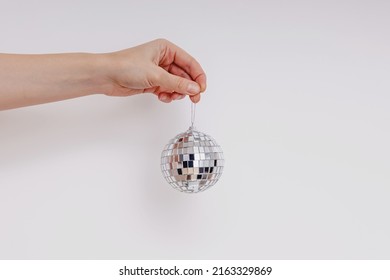 Woman's Hand Holding Decorative Silver Disco Ball Over The White Wall. Minimalist Decor.