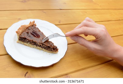 Woman's hand holding fork to cut into a slice of traditional pecan pie