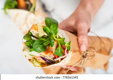 Woman's Hand Holding A Fresh Tortilla Wrap Tied Round With Brown Paper And String. Gourmet Conception.