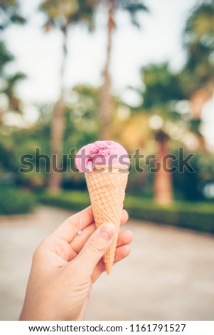 Woman's hand holding fruit ice cream in waffle cone against the palm trees.