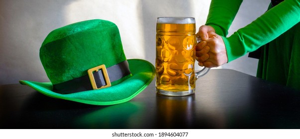 Woman's hand holding glass of beer near St. Patrick's day hat of a leprechaun on the black background