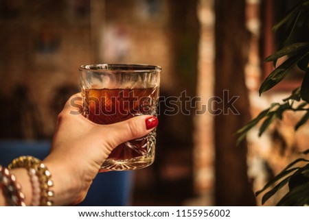 Woman's hand holding glass of black cold brew coffee with ice. Hipster coffee shop. Minimalism drink photography from above. Warm tones image