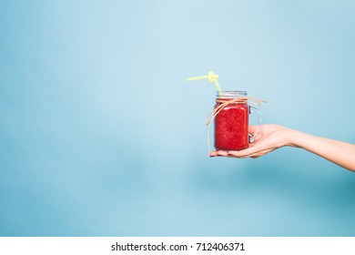 Woman's Hand Holding Glass Of Strawberry And Rasberry Smoothie On Blue Background