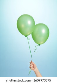 A Woman's Hand Holding A Green Balloon In A Sky Blue Background