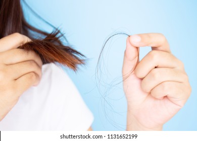 Woman's hand holding hair falling from her head in white t-shirt with blue background. Young Asian female age between 25-35 years old