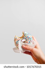 Woman's Hand Is Holding A Half Eaten Bagel In Front Of White Background. Sweetness And Happiness Concept. 