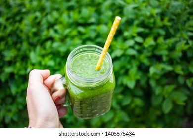woman's hand holding a jar with green cold-pressed juice, nature background. Healthy eating, detoxing, juicing, body cleancing concept 