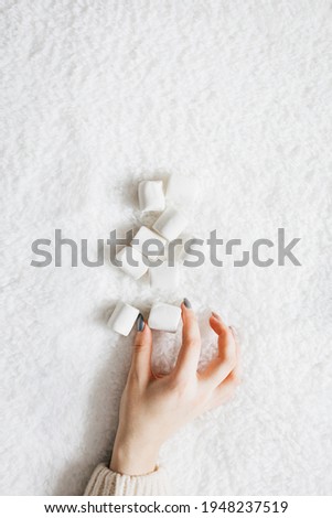 Woman's hand holding marshmallows on white plaid background
