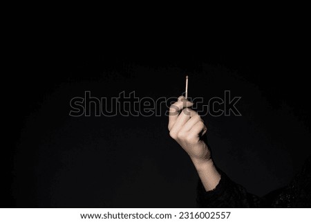 Woman's hand holding match on black background.