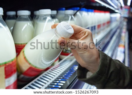Womans hand holding milk bottle in supermarket. Man shopping milk in grocery store. Man checks product expiration date before buying it. Close-up. Foto d'archivio © 