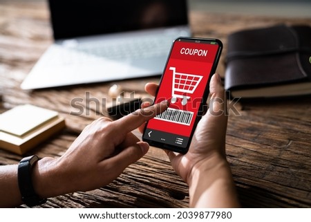 Woman's Hand Holding Mobile Phone With Shopping Coupon