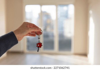 Woman's hand holding new house key, empty living room of apartment for sale or rent in background. Real estate, house rental, housing sale and mortgage concepts. Horizontal close up. - Powered by Shutterstock