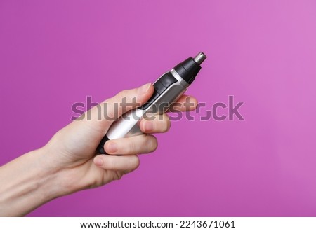 Woman's hand holding a nose trimmer on a purple background