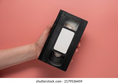 Woman's hand holding old video tape on pink background. VHS video tape.