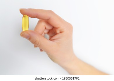Woman's hand holding Omega 3 capsule isolated on white background. Close up. High resolution product.fish oil is a dietary supplement derived from liver of cod fish, have omega-3 fatty acids, EPA, DHA