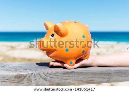 woman's hand holding piggy bank by the beach