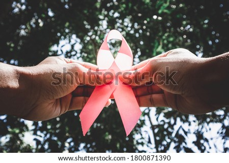 Woman's hand holding a pink ribbon with light of hope.Concept: Breast Cancer Awareness.