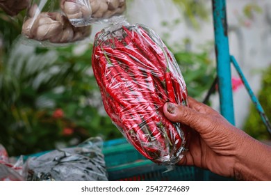 Woman's hand holding a plastic bag of red chili vegetables - Powered by Shutterstock