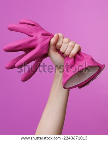 Woman's hand holding rubber cleaning gloves on purple background