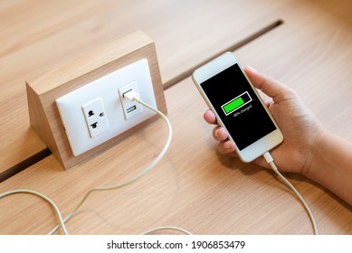 Woman's hand holding smart phone and charging battery from built in usb socket on the table