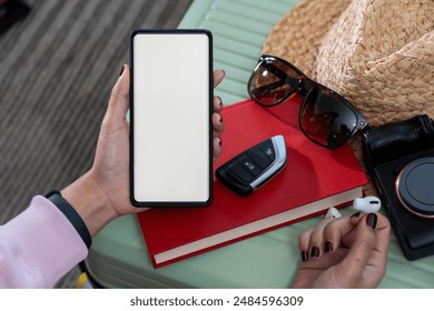 A woman's hand holding a smartphone with a white screen, along with clothes being packed into a suitcase in preparation for a weekend trip - Powered by Shutterstock