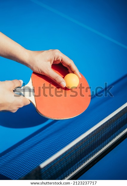 A woman\'s hand holding a table tennis racket next to\
the net