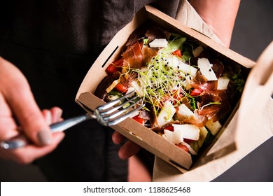Woman's hand is holding a take away fresh salad in a lunch box. Gourmet conception.