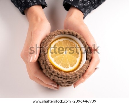 woman's hand holding teacup with lemon slice in both hands