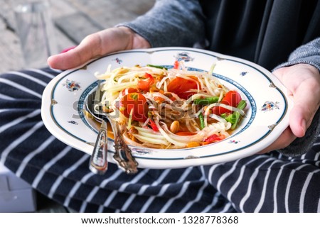 Woman's hand holding Thai green papaya salad in a dish, Somtam is very famous in Thailand. Thai spicy food