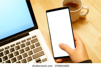 Woman's hand holding  and touching blank screen of smartphone with computer laptop and tea cup in beautiful cafe. Future mobile technology and applications mockup concept. Close up. - Powered by Shutterstock