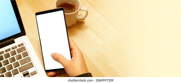 Woman's hand holding  and touching blank screen of smartphone with computer laptop and tea cup in beautiful cafe. Future mobile technology and applications mockup concept. Close up. - Powered by Shutterstock