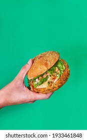 woman's hand holding a vegan burger on a green background