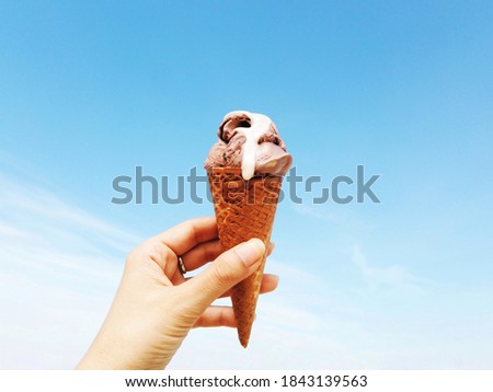 Woman's hand holding wafer cone of chocolate ice cream against bright blue sky background on a sunny day