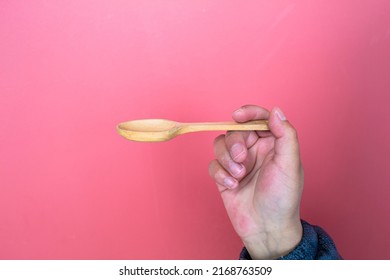 Woman's Hand Holding A Wooden Spoon Isolated, On Red Background. Food Concept