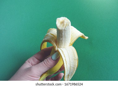A woman's hand holds a bitten banana on a green background close up. Healthy food.                       