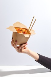 Woman's Hand Holds A Box Of Noodles. Asian Cuisine