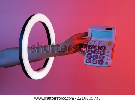 Woman's hand holds calculator through led ring lamp in red blue neon gradient light. Creative idea.
