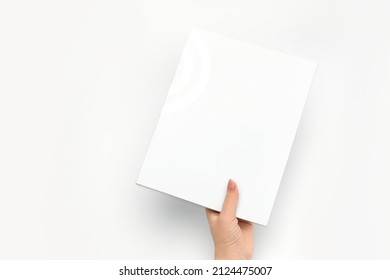 A Woman's Hand Holds A Closed Book With A Blank White Cover On A White Background.