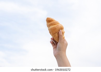 A woman's hand holds a croissant with a bright sky background.
Delicious croissant concept The best of deliciousness, success