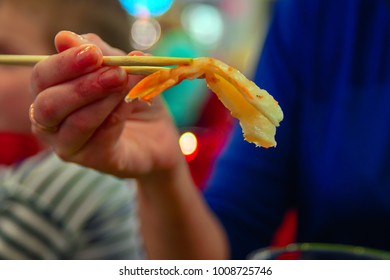 Woman's hand holds a large shrimp in chopsticks. - Shutterstock ID 1008725746