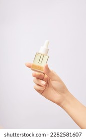 Woman's hand holds mock-up of dropper bottle on white background. Glass bottle without label containing light yellow essence. Space for design, concept of skin care.